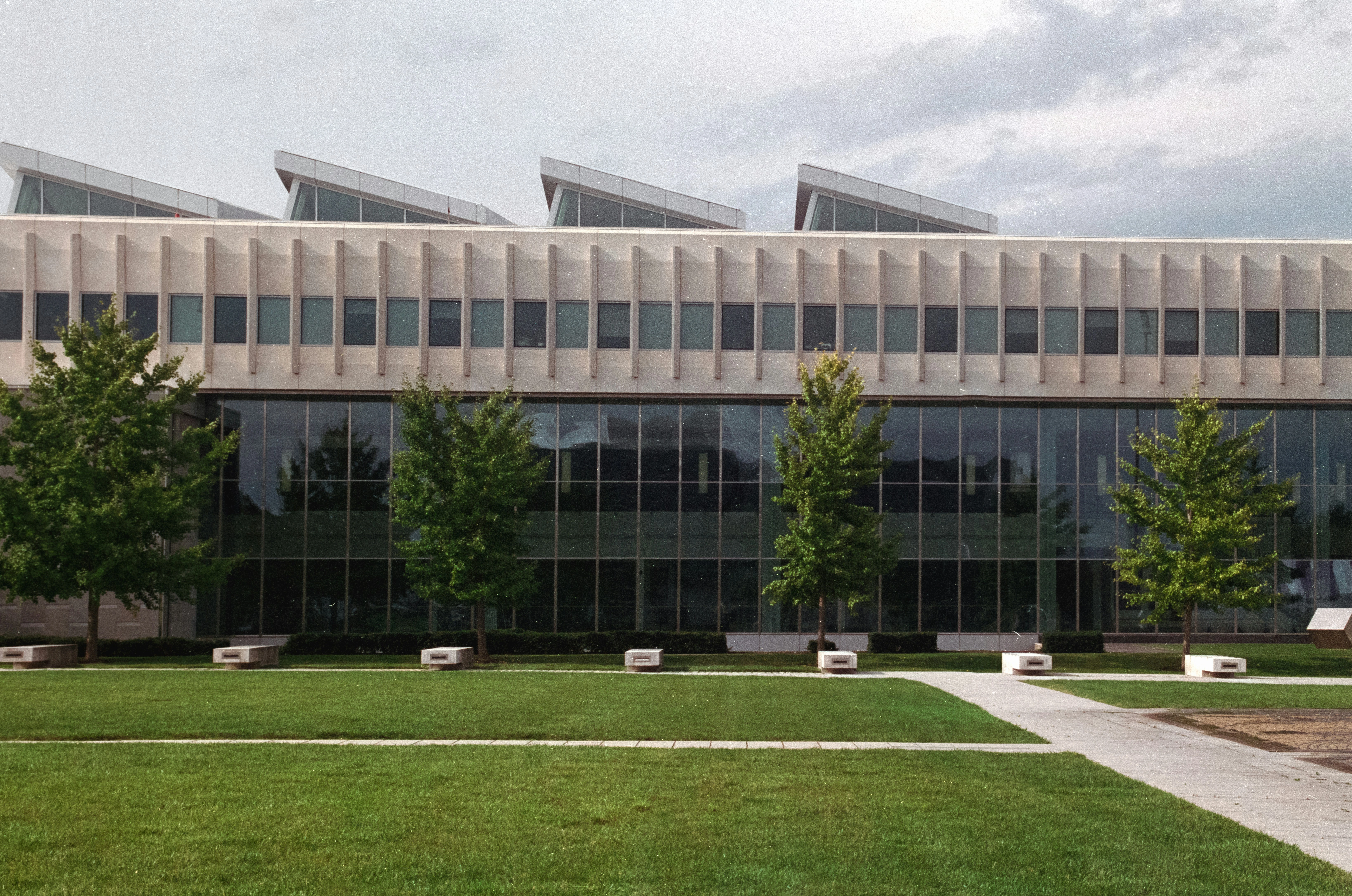 Contemporary academic building with a modern facade and large glass windows, surrounded by a green lawn and trees.