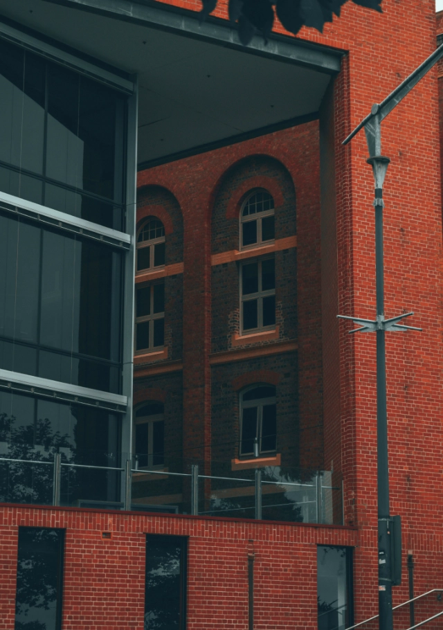 Modern red brick building with large windows and an industrial design, featuring a street lamp in the foreground.